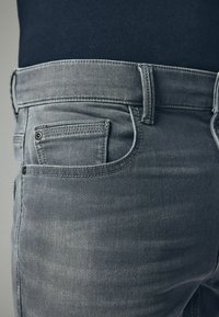 Szare dżinsy o klasycznym pięciopocketowym designie, widocznym szwie i delikatnie teksturowanym wykończeniu. Pętle na pasek obszyte w talii.