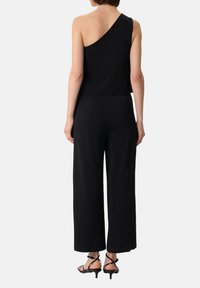 Schwarzer Jumpsuit mit einseitigem Design, weit geschnittenem Bein und weicher Textur. Verfügt über einen Träger und einen sauberen Saumabschluss.