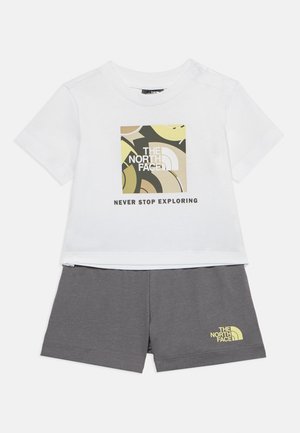 Tricou alb pentru copil mic cu logo abstract North Face și textul "Nu te opri niciodată din explorare", asortat cu pantaloni scurți gri închis, cu un logo mic.