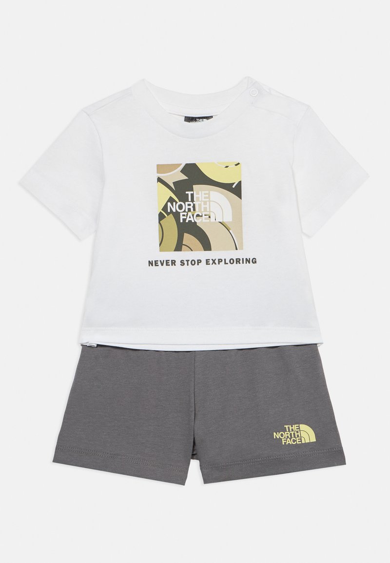 Λευκό παιδικό t-shirt με αφηρημένο λογότυπο North Face και το κείμενο "Never Stop Exploring", σε συνδυασμό με σκούρο γκρι σορτς που φέρει μικρό λογότυπο.