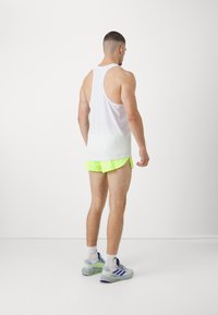 Herre sporty outfit, der består af en hvid tanktop, lyse neon gule shorts og grå sneakers med grønne detaljer. Enkel og funktionel design.