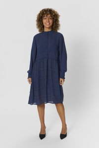 Abito blu navy con colletto alto, apertura con bottoni, maniche lunghe e vita arricciata. Realizzato in tessuto leggero con una sottile trama a righe.