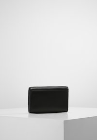 Czarna skórzana torebka o prostokątnym kształcie, gładkiej teksturze, minimalistycznym designie i subtelnych detalach ściegów.