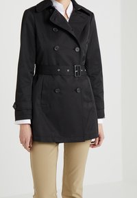 Svart dubbelknäppt trench coat med bälte, knappdetaljer och rak skärning. Tillverkad av smidig tyg, med krage och sidofickor.