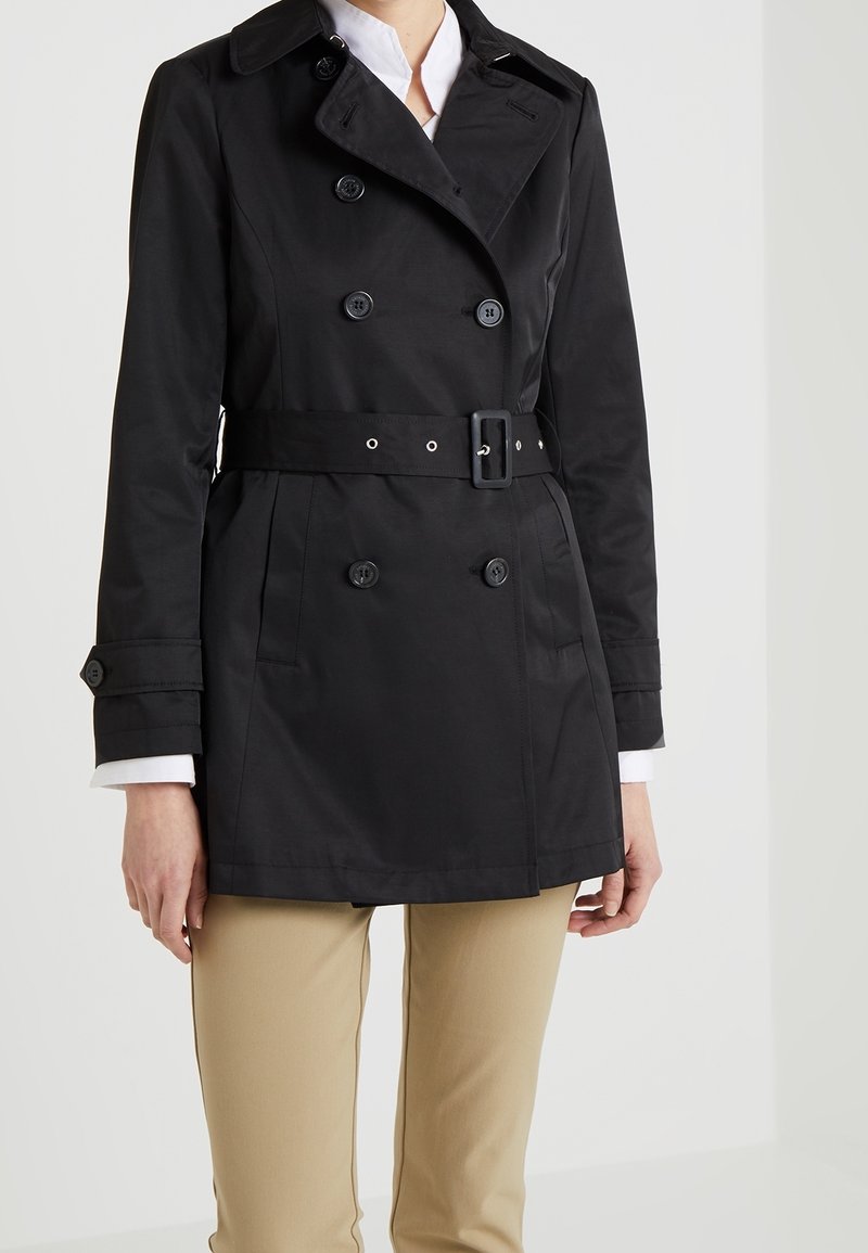 Svart dubbelknäppt trench coat med bälte, knappdetaljer och rak skärning. Tillverkad av smidig tyg, med krage och sidofickor.