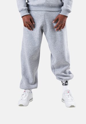 Gray sweatpants with a relaxed fit, featuring a ribbed waistband and cuffs, paired with white sneakers and black-and-white branded socks.