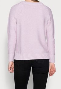 Suéter de punto rosa claro que presenta un patrón de punto texturizado, puños y dobladillo de canalé, y un escote redondo. Mangas largas con costuras raglán.