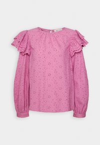 Blouse rose à manches longues en tissu ajouré, détails volants aux épaules et poignets froncés sur un fond clair uni.