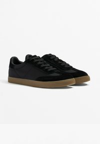 Black sneakers made of suede and synthetic material, featuring a low-top design, round toe, and gum rubber outsole with textured laces.