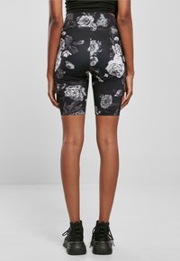 Sorte sykkelshorts med blomsterdesign, høy livhøyde, med hvite rosemønstre og et glatt, elastisk stoff.