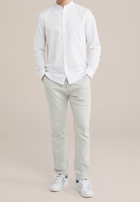 Vit långärmad skjorta med knappar och mandarin-krage, kombinerad med ljusgrå byxor och vita sneakers med gröna detaljer.