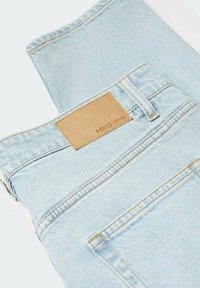Jean en denim bleu clair plié montrant la poche arrière et l’étiquette marron MNG Denim au-dessus de la ceinture.