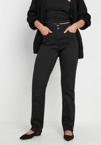 Svart högmidjade jeans med smal passform, inklusive två framfickor och knappstängning. Matchas med en texturerad svart cardigan och platta skor.