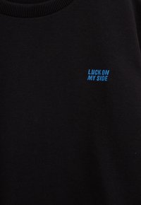 Hanorac negru cu guler cu nervuri și textul "LUCK ON MY SIDE" brodat în litere albastre pe partea stângă.