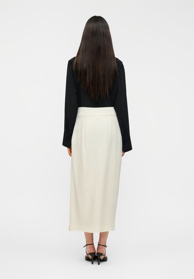 Μαύρο μακρυμάνικο μπλουζάκι με λεπτομέρεια στους ώμους σε συνδυασμό με κρεμ φούστα μέχρι τους αστραγάλους και μαύρα παπούτσια με τακούνι. Ομαλό ύφασμα, απλός σχεδιασμός.