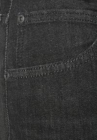 Calças de ganga pretas com um close-up da textura do tecido, com um bolso visível e detalhes de costura em contraste.