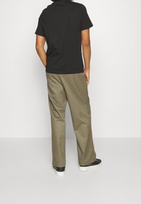 Černé bavlněné tričko s krátkým rukávem, spárované s volně střiženými olivově zelenými kalhotami, nošené s černou obuví a bílou podrážkou.