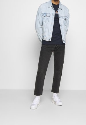 Light blue denim jacket over a navy t-shirt, paired with dark grey straight-leg jeans and white sneakers.