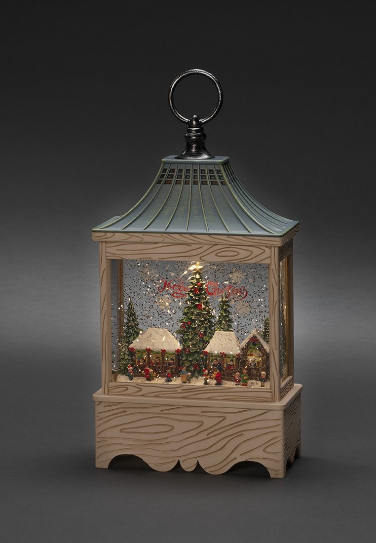 Farolillo de Navidad con una escena de un pueblo nevado, árboles decorados, pequeñas figuras y purpurina dentro de un marco de madera y metal.