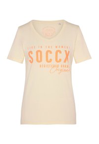 Camiseta de manga corta color amarillo claro con escote en V. Presenta texto en naranja: "VIVE EN EL MOMENTO SOCcx MARCA REGISTRADA Original." Tejido suave.