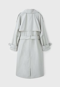 Trench-coat long gris clair avec large ceinture, épaulettes, rabat de dos contre la tempête et poignets bouclés, vu de dos.