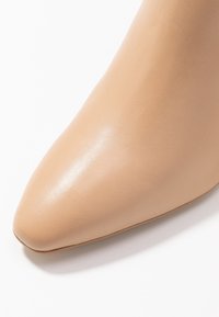 Beige leather pointed-toe shoe featuring a smooth texture and subtle shine. The design is sleek with a minimalistic profile and no visible accents.
