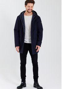 Veste imperméable bleu marine avec fermeture éclair à l'avant et capuche, dotée d'une doublure à motifs et de deux poches latérales, associée à un pantalon noir slim.