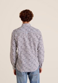 Langsemig overhemd met een witte stof en een blauw-paarse bladerenpatroon. Standaard kraag, rechte onderzoom en knoopmanchetten.