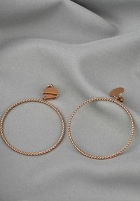Roségoldene, verdrehte Creolen mit strukturiertem Finish und sicherem Steckverschluss, präsentiert auf einem grauen Stoffhintergrund.
