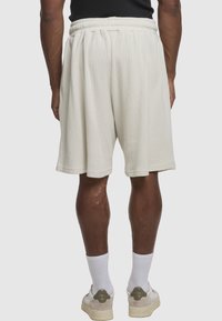 Lyse beige, teksturerede shorts med elastisk talje, der går til over knæet. Kombineret med hvide sokker og afslappede sko.