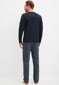 Herrenschlafanzug bestehend aus einem langärmligen Oberteil in Marineblau und gestreiften Hosen in Marineblau und Weiß. Der Stoff wirkt weich und hat eine lässige Passform.