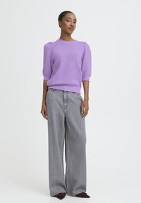 Lavendelfarbener Strickpullover mit strukturiertem Muster und kurzen Ärmeln, kombiniert mit hoch taillierter, weit geschnittener grauer Jeans aus Denim und dunkelbraunen Schuhen.