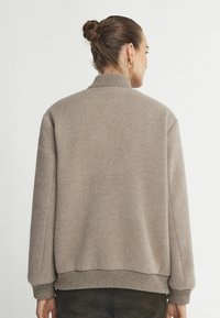 Beżowy polarowy sweter z wysokim kołnierzem i ściągaczami. Charakteryzuje się luźnym krojem i miękką teksturą, idealny do codziennego noszenia.