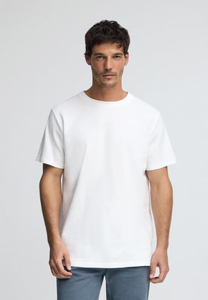 Witte katoenen t-shirt met ronde hals en korte mouwen, met een minimalistisch ontwerp en een klein stoffen label aan de onderkant.