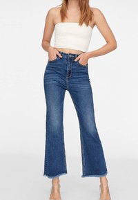 Jean évasé taille haute en denim bleu foncé avec un ourlet brut, comprenant cinq poches et des coutures contrastantes. Texture lisse avec une décoloration minimale.