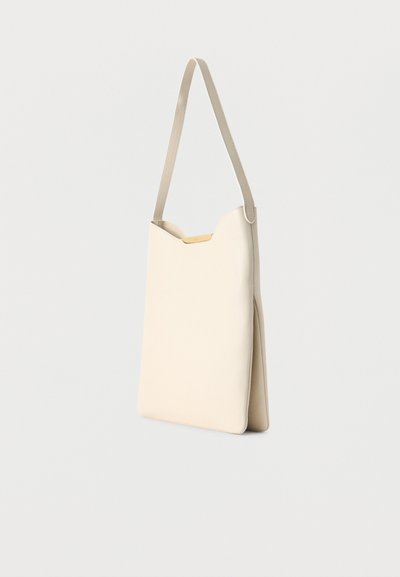 Μπεζ μίνιμαλ τσάντα ώμου με έναν ιμάντα και ελαφρώς κυρτή άνω άκρη πάνω σε απλό λευκό φόντο.