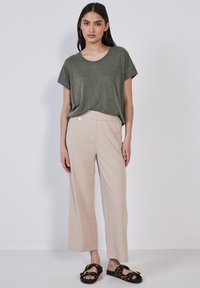 T-shirt verde oliva morbido e dal taglio ampio, pantaloni beige a gamba larga e sandali neri con accenti in stampa leopardata. Tessuto morbido, design rilassato.