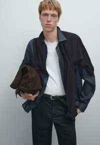 Camicia di jeans blu sovrapposta a un maglione scuro, T-shirt bianca, borsa di stoffa marrone, pantaloni neri e una cintura intrecciata. Linee e trame semplici e pulite.