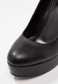 Chaussure à talon haut à plateforme en cuir noir avec bout rond et finition lisse, vue en gros plan de face.