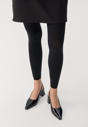 Leggings neri abbinati a décolleté neri con punta affilata e tacco a blocco. I materiali sembrano lucidi e raffinati.