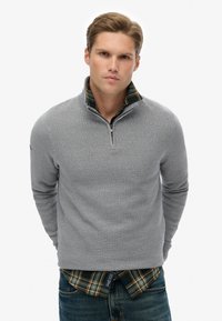 Lichtgrijze gebreide pullover met een halvemaan-rits kraag, gedragen over een groen en geruit overhemd, met lange mouwen en een gestructureerd patroon.