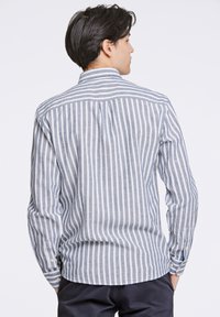 Gestreept shirt met dunne witte en donkerblauwe afwisselende strepen. Voorzien van een button-down kraag en mouwdetails in een lichtgewicht stof.