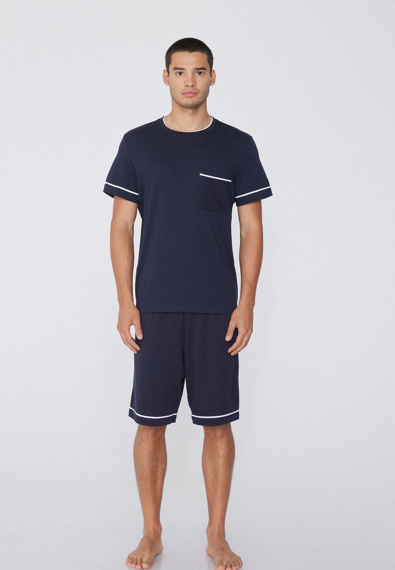Ensemble de pyjama bleu marine comprenant une chemise à manches courtes avec une poche poitrine et des accents blancs, associée à un short de longueur genou, le tout en tissu doux.