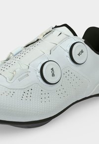 Chaussure de cyclisme blanche avec deux fermoirs à cadran BOA et des trous de ventilation perforés sur la surface supérieure et une semelle noire.