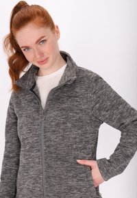 Harmaa fleece-takki, jossa on täysi vetoketju, korkea kaulus ja kaksi sivutaskua. Tekstuuriltaan pehmeä, hieman marled-pintainen.
