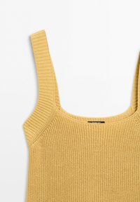 Haut sans manches tricoté jaune moutarde avec larges bretelles et encolure dégagée, montrant un tissu texturé et une étiquette de marque à l'intérieur.
