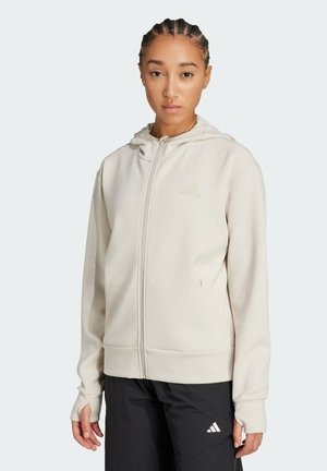 Beige zip-up hoodie with a smooth texture, featuring an adjustable hood, front pockets, and a subtle logo on the chest.