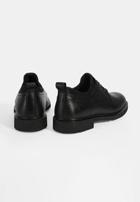 Chaussures en cuir noir avec une finition texturée, bout rond et semelle plate en caoutchouc. Présente un design minimaliste et un tirant à l'arrière.