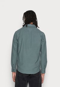Lang mouw shirt in gedempte teal stof, met een recht gesneden zoom, knoopmanchetten en een klassieke kraag, weergegeven van achteren.