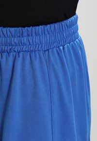 Modré sportovní kalhoty s elastickým pasem, vyrobené z hladké látky. Design je jednoduchý, bez viditelných vzorů nebo akcentů.